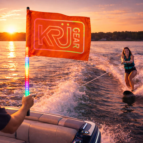 Person water skiing with a colorful KRÜGEAR flag on a lake at sunset