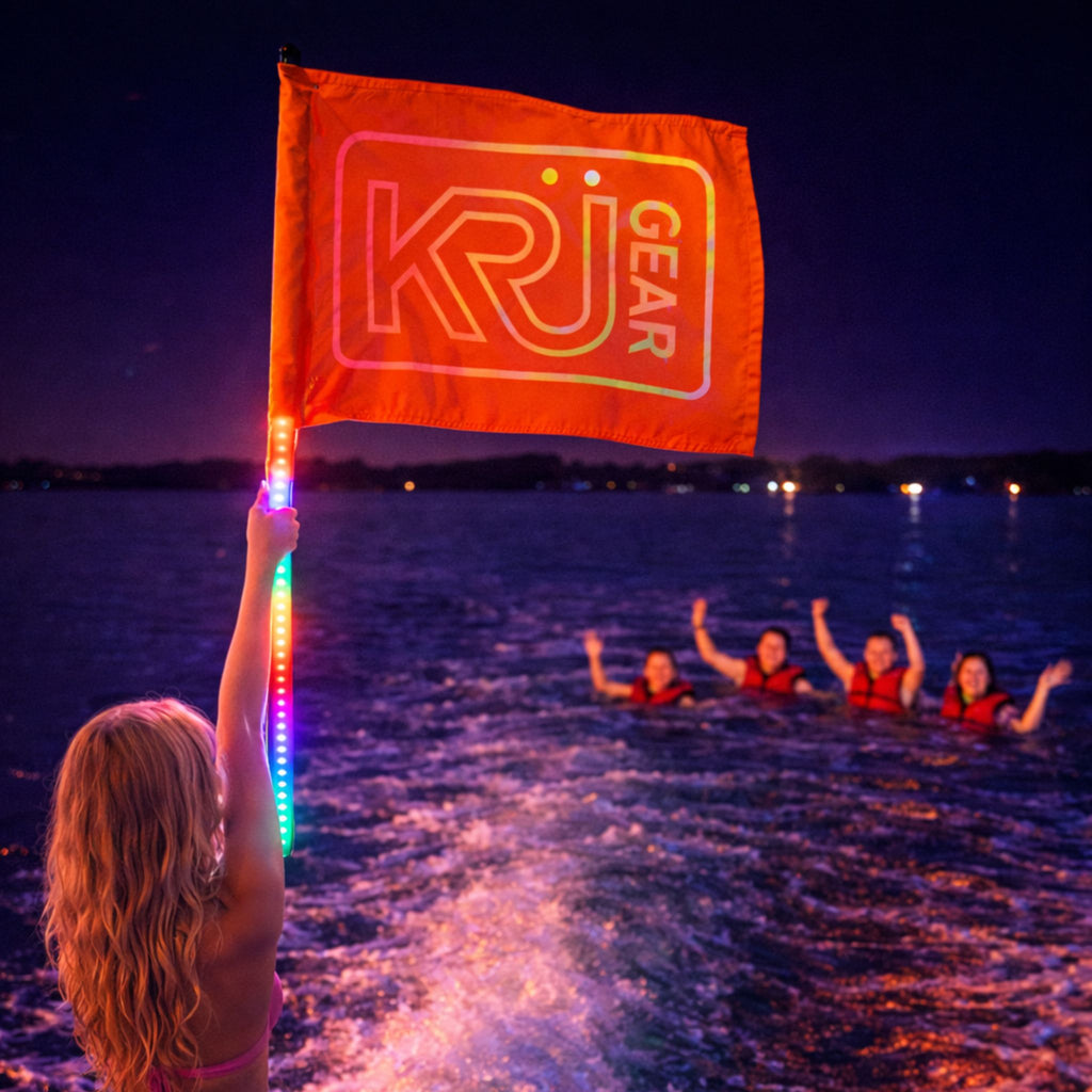 Person holding a glowing 'KRÜGEAR' flag over water at night with people in the water below.
